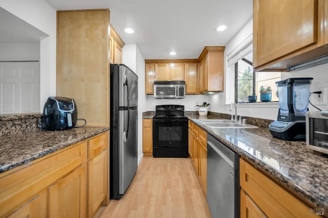 kitchen featuring appliances with stainless steel finishes, sink, dark stone countertops, and light hardwood / wood-style flooring