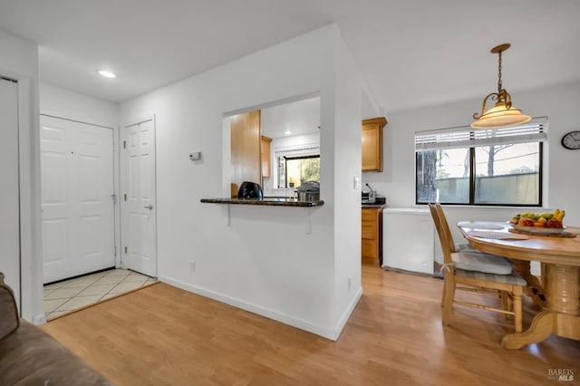 kitchen featuring decorative light fixtures, a wealth of natural light, kitchen peninsula, and light hardwood / wood-style flooring