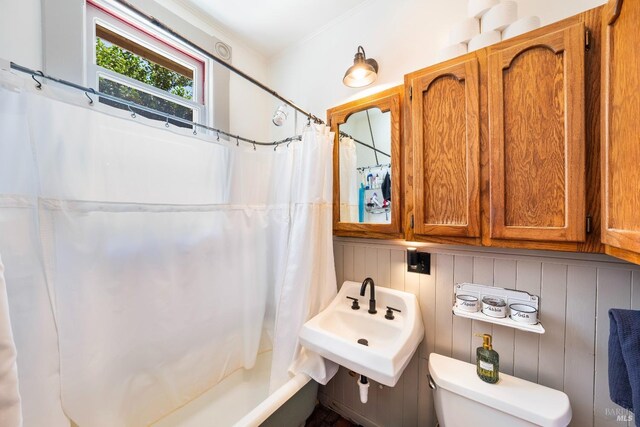 full bathroom featuring wooden walls, shower / bathtub combination with curtain, toilet, and sink