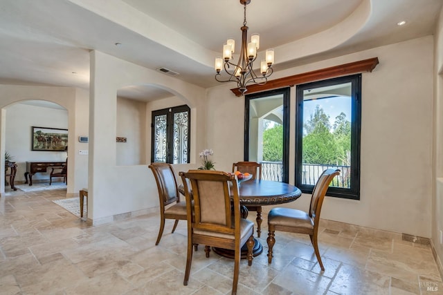 dining room with a raised ceiling, a healthy amount of sunlight, a notable chandelier, and french doors