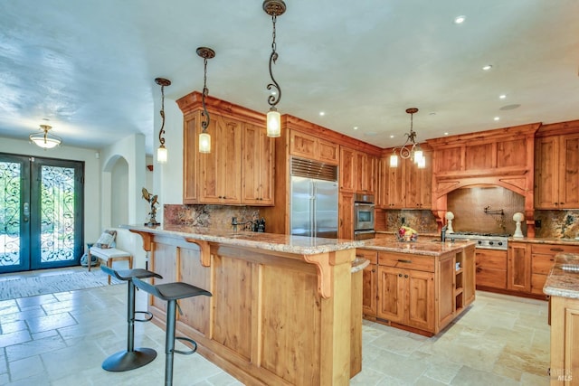 kitchen with a breakfast bar, stainless steel appliances, light stone countertops, decorative light fixtures, and kitchen peninsula