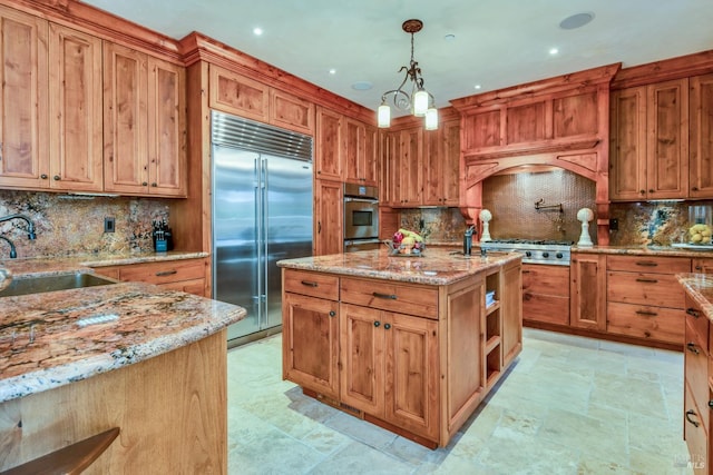 kitchen with sink, stainless steel appliances, light stone counters, an island with sink, and decorative light fixtures