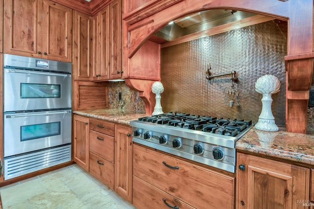 kitchen with light stone counters, stainless steel appliances, range hood, and backsplash