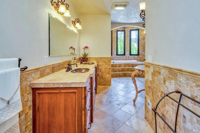 bathroom featuring tiled tub, vanity, and tile walls