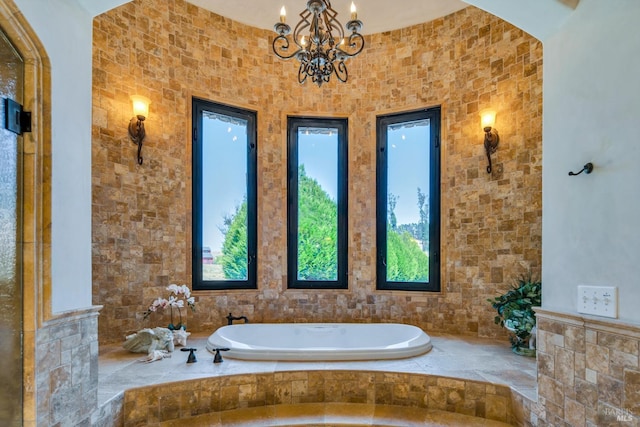 bathroom with a notable chandelier and tiled bath