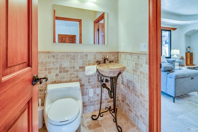 bathroom with toilet, sink, and tile walls