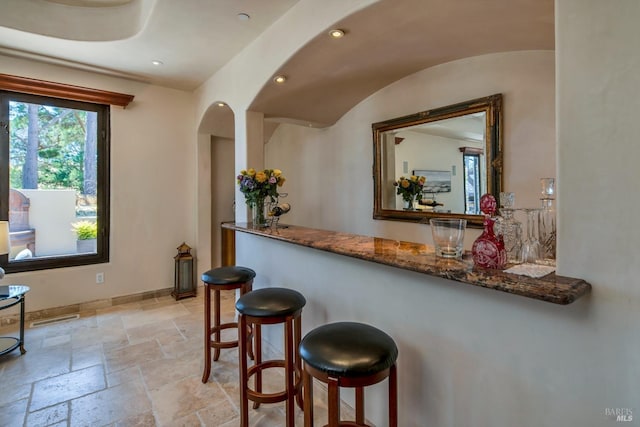 bar featuring vaulted ceiling and dark stone counters