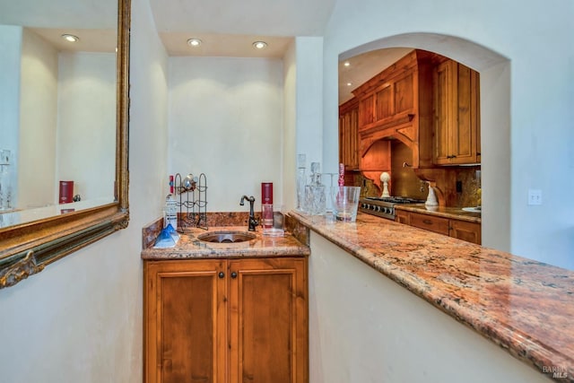 kitchen with tasteful backsplash, light stone countertops, sink, and range