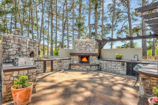 view of patio featuring an outdoor kitchen, sink, and an outdoor stone fireplace