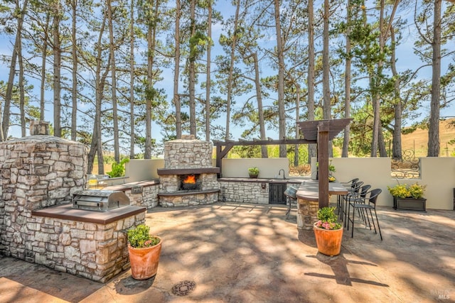 view of patio / terrace featuring grilling area, sink, and an outdoor stone fireplace