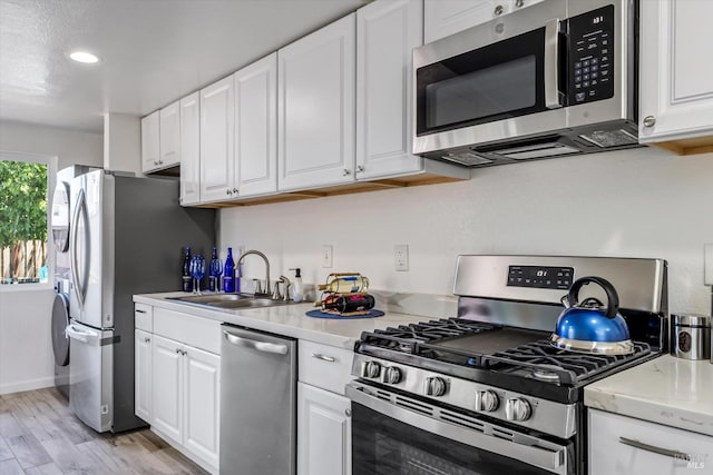 kitchen with sink, light hardwood / wood-style flooring, stainless steel appliances, light stone counters, and white cabinets