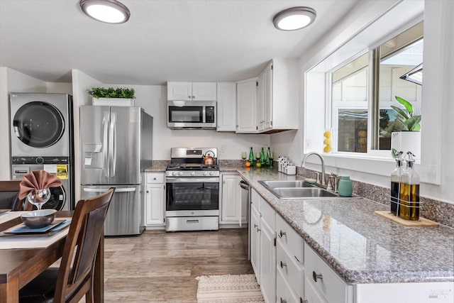 kitchen with sink, dark wood-type flooring, appliances with stainless steel finishes, stacked washer / drying machine, and white cabinets