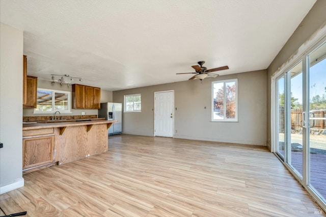 kitchen featuring light wood-style flooring, a breakfast bar area, brown cabinets, open floor plan, and stainless steel refrigerator with ice dispenser