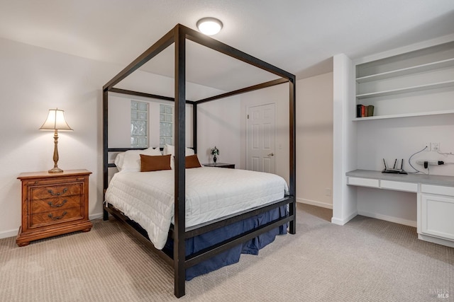 bedroom featuring light carpet, built in desk, and baseboards