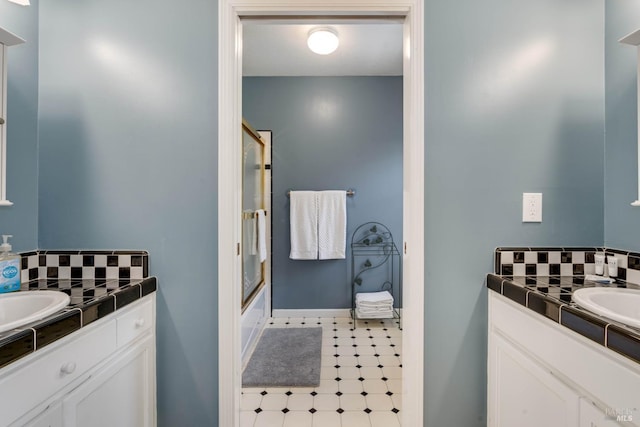 full bath featuring a sink, shower / bath combination with glass door, tasteful backsplash, and two vanities