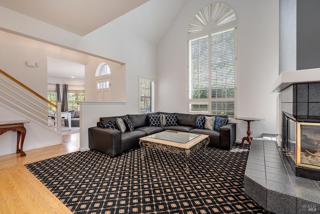 living area featuring baseboards, a tiled fireplace, wood finished floors, stairs, and high vaulted ceiling