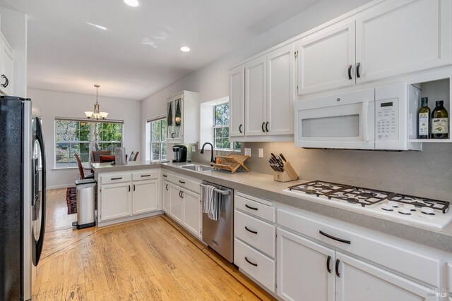 kitchen with white cabinetry, sink, stainless steel appliances, a chandelier, and pendant lighting