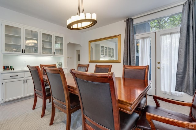 dining room with arched walkways, french doors, light colored carpet, and an inviting chandelier