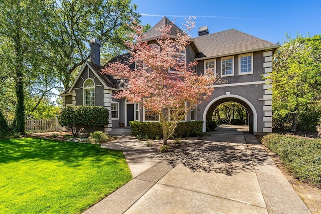 view of front of property featuring fence, driveway, stucco siding, a front lawn, and a chimney