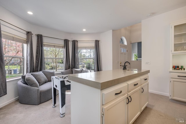 kitchen with sink, light colored carpet, white cabinetry, and an island with sink