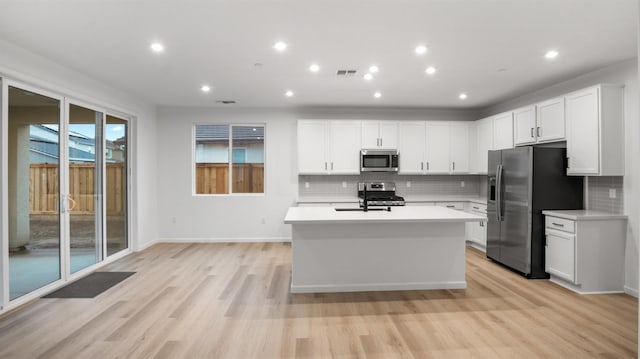 kitchen featuring white cabinetry, a center island with sink, light wood-type flooring, stainless steel appliances, and backsplash