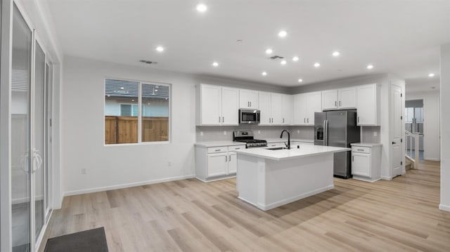 kitchen with sink, a kitchen island with sink, white cabinetry, stainless steel appliances, and light hardwood / wood-style floors