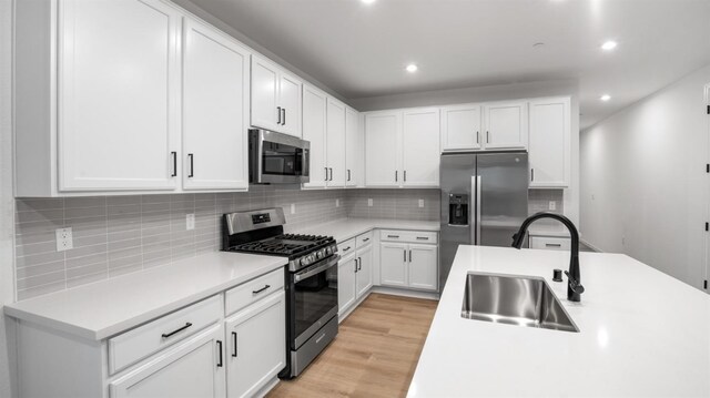 kitchen featuring sink, white cabinetry, light hardwood / wood-style flooring, appliances with stainless steel finishes, and decorative backsplash