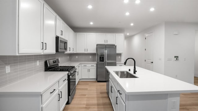 kitchen with appliances with stainless steel finishes, sink, a kitchen island with sink, and white cabinets