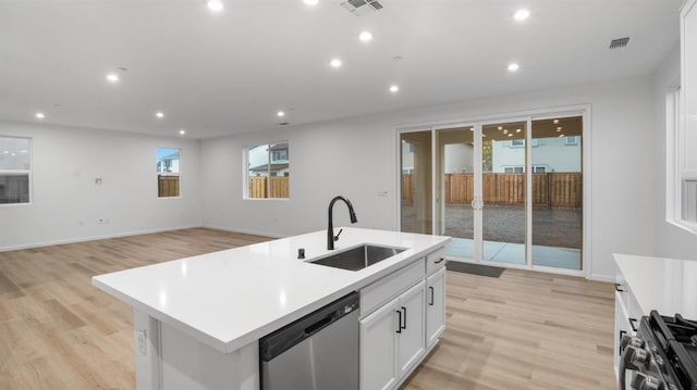 kitchen featuring light wood-type flooring, stainless steel appliances, white cabinets, sink, and a kitchen island with sink