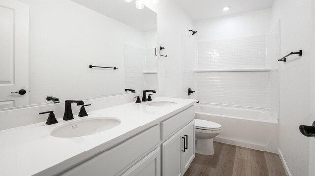 full bathroom with hardwood / wood-style floors, toilet, vanity, and washtub / shower combination