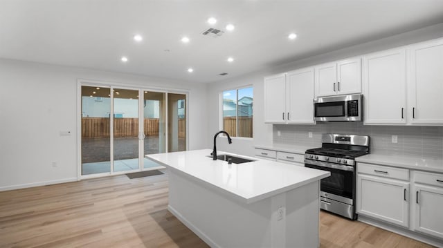 kitchen featuring sink, stainless steel appliances, an island with sink, white cabinets, and light wood-type flooring