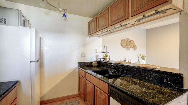 kitchen with a sink, dark stone counters, brown cabinets, and freestanding refrigerator