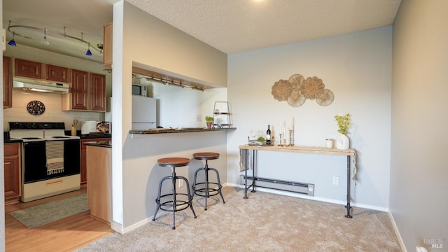 kitchen featuring range with electric cooktop, under cabinet range hood, dark countertops, a breakfast bar area, and baseboard heating