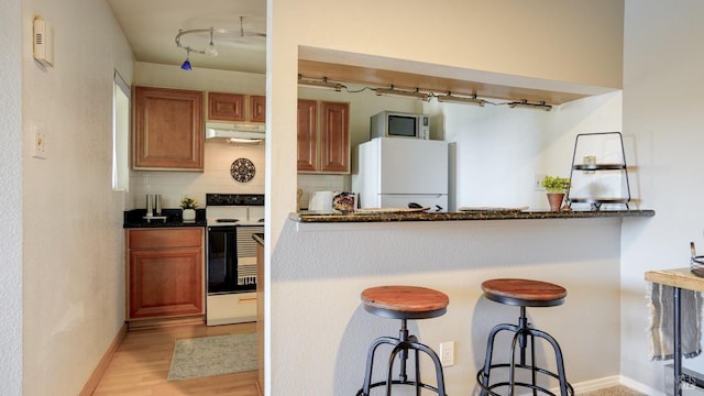 kitchen with freestanding refrigerator, under cabinet range hood, range with electric stovetop, stainless steel microwave, and backsplash