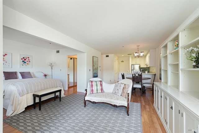 bedroom with light hardwood / wood-style floors, an inviting chandelier, and stainless steel fridge
