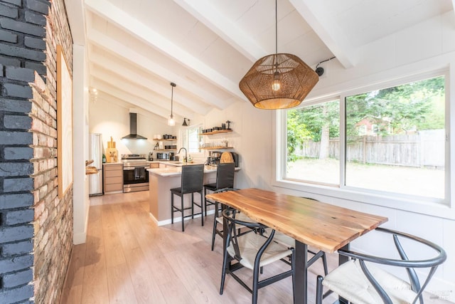 dining area featuring sink, light hardwood / wood-style flooring, and lofted ceiling with beams