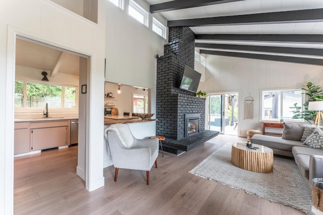 living room featuring sink, high vaulted ceiling, light hardwood / wood-style floors, a brick fireplace, and beamed ceiling