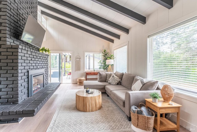 living room with lofted ceiling with beams, a brick fireplace, and light hardwood / wood-style flooring