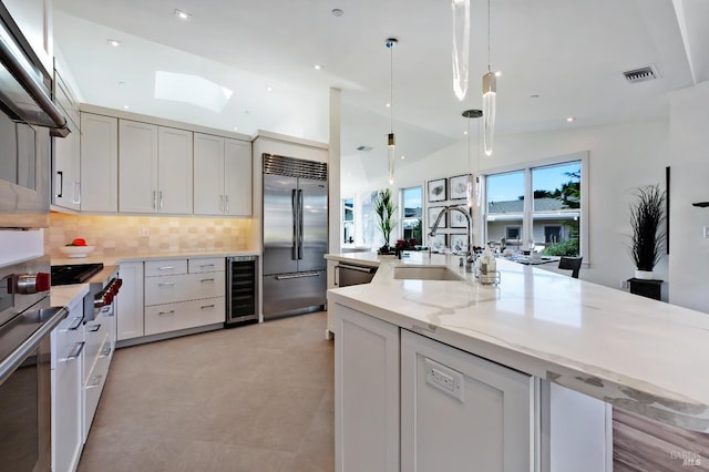 kitchen with pendant lighting, sink, appliances with stainless steel finishes, wine cooler, and light stone counters