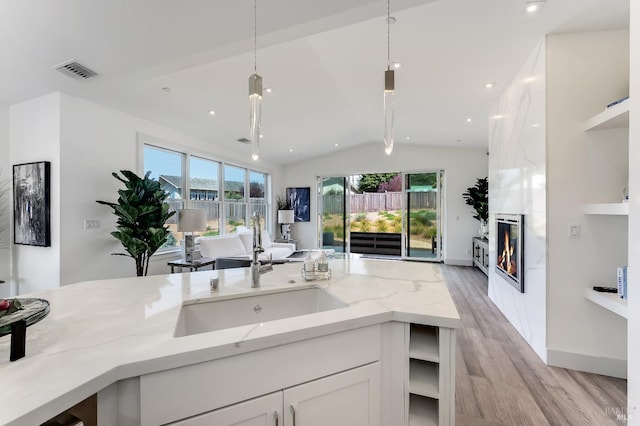 kitchen with white cabinetry, sink, hanging light fixtures, light stone counters, and a healthy amount of sunlight