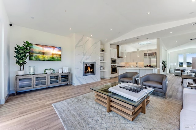 living room featuring sink, a high end fireplace, vaulted ceiling, and light wood-type flooring