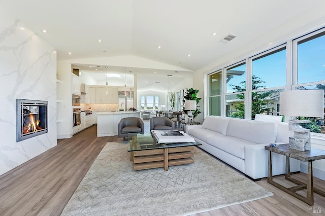 living room featuring lofted ceiling, sink, light hardwood / wood-style floors, and a premium fireplace