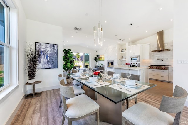 dining room with sink, vaulted ceiling, a premium fireplace, and light wood-type flooring