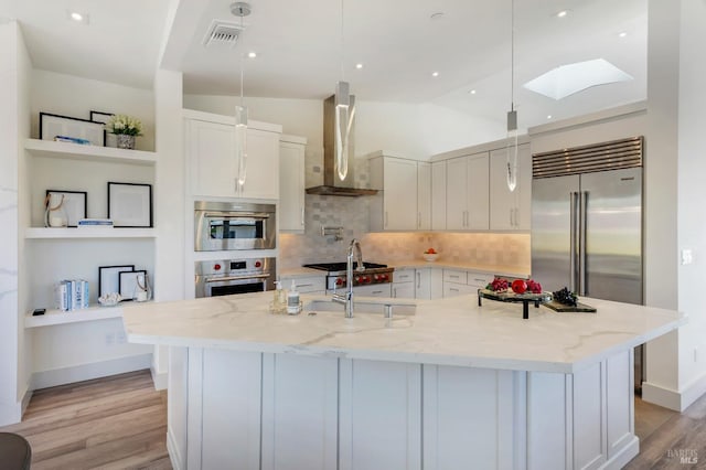 kitchen featuring pendant lighting, wall chimney exhaust hood, a large island, and light stone countertops