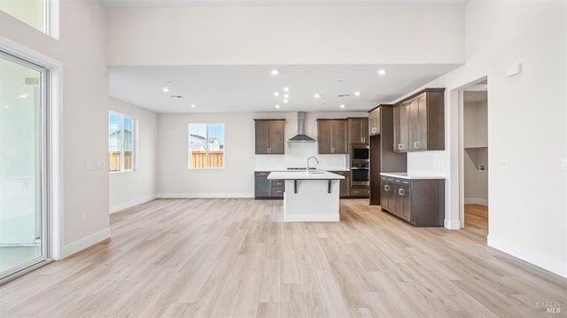 kitchen featuring a center island with sink, light hardwood / wood-style flooring, sink, wall chimney range hood, and dark brown cabinets