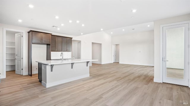 kitchen featuring light wood-type flooring, dark brown cabinetry, a breakfast bar, sink, and a kitchen island with sink