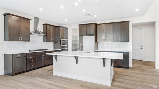 kitchen featuring sink, a center island with sink, stainless steel appliances, and wall chimney exhaust hood