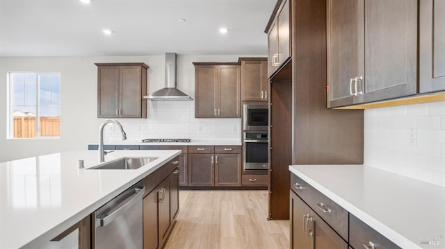 kitchen featuring light hardwood / wood-style floors, sink, tasteful backsplash, appliances with stainless steel finishes, and wall chimney range hood