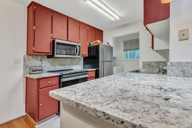 kitchen featuring backsplash, a textured ceiling, stainless steel appliances, sink, and light hardwood / wood-style flooring