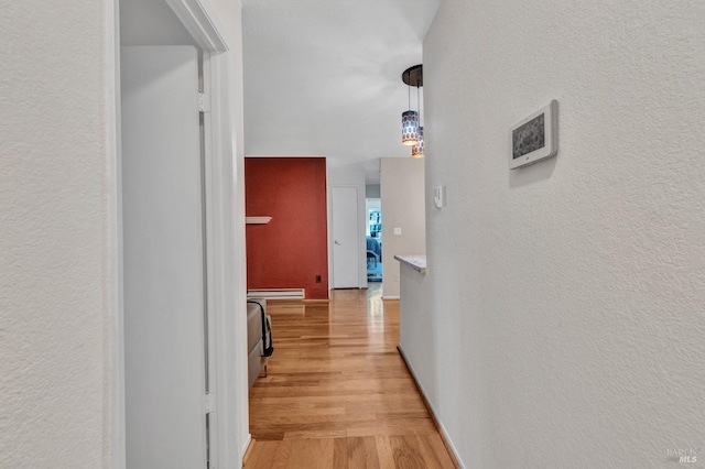 hallway with a baseboard heating unit and light hardwood / wood-style flooring